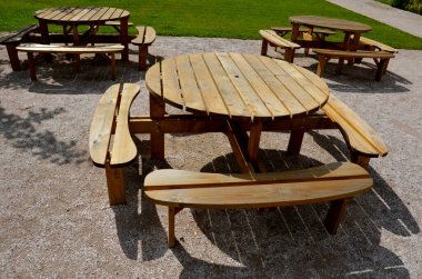 Pergola, bahçe köşkünde metal bir ızgara var. Parktaki umumi barbekü yerinde. Ahşap kamp masaları. Parktaki bej çakıl dinlenme alanının etrafındaki çimenler, yeni, bahar, çember