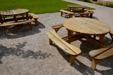 Pergola, bahçe köşkünde metal bir ızgara var. Parktaki umumi barbekü yerinde. Ahşap kamp masaları. Parktaki bej çakıl dinlenme alanının etrafındaki çimenler, yeni, bahar, çember