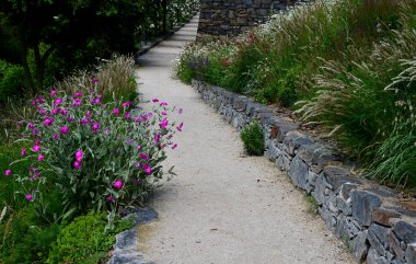 Yokuş aşağı kestirme yol. Yolun üstünde ve altında taş bir duvar var. Sonbahar parkında kanalizasyon ve metal şebeke ile doğa izleri. Her yıl kuraklık sarısı ile kaplanmış yamaçlar