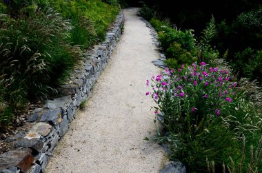 Yokuş aşağı kestirme yol. Yolun üstünde ve altında taş bir duvar var. Sonbahar parkında kanalizasyon ve metal şebeke ile doğa izleri. Her yıl kuraklık sarısı ile kaplanmış yamaçlar