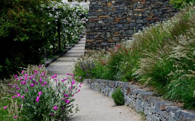 Yokuş aşağı kestirme yol. Yolun üstünde ve altında taş bir duvar var. Sonbahar parkında kanalizasyon ve metal şebeke ile doğa izleri. Her yıl kuraklık sarısı ile kaplanmış yamaçlar