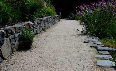Yokuş aşağı kestirme yol. Yolun üstünde ve altında taş bir duvar var. Sonbahar parkında kanalizasyon ve metal şebeke ile doğa izleri. Her yıl kuraklık sarısı ile kaplanmış yamaçlar
