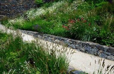 Yokuş aşağı kestirme yol. Yolun üstünde ve altında taş bir duvar var. Sonbahar parkında kanalizasyon ve metal şebeke ile doğa izleri. Her yıl kuraklık sarısı ile kaplanmış yamaçlar