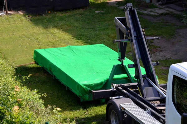 A properly covered pile of cut grass from the garden maintenance on the container is ensured by the transport and loading of the container onto the truck. gardening services