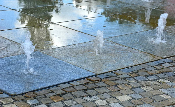 water showers with stainless steel quarter jets. water features come directly from the cobbled square. circular groove around the center, town square, mosaic grid fountain