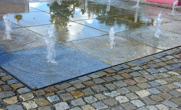 water showers with stainless steel quarter jets. water features come directly from the cobbled square. circular groove around the center, town square, mosaic grid fountain