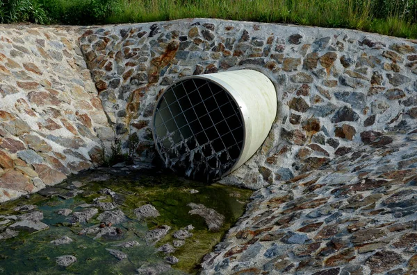 stone lining of bank at the mouth of the sewer pipe with a grate against the entry of persons into the treatment plant or industrial building. leftover toilet paper was trapped on the grille