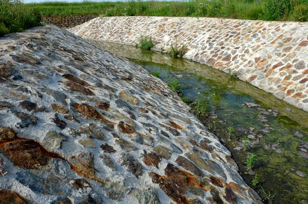 stone lining of bank at the mouth of the sewer pipe with a grate against the entry of persons into the treatment plant or industrial building. leftover toilet paper was trapped on the grille