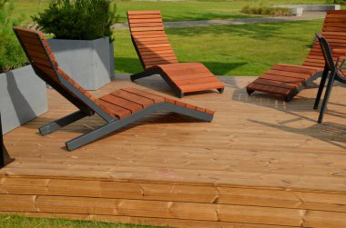 Meydandaki ağaçların altındaki kaldırımda sallanan sandalye. Parktaki tek bir kişi için tropikal ahşaptan yapılmış ahşap sandalyeler. Kahverengi kalaslar, çatallar, çelik çerçeveler ve çam ağacından yapılmışlar.