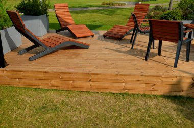 Meydandaki ağaçların altındaki kaldırımda sallanan sandalye. Parktaki tek bir kişi için tropikal ahşaptan yapılmış ahşap sandalyeler. Kahverengi kalaslar, çatallar, çelik çerçeveler ve çam ağacından yapılmışlar.