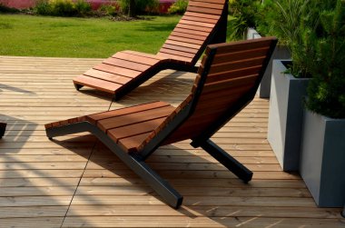 Meydandaki ağaçların altındaki kaldırımda sallanan sandalye. Parktaki tek bir kişi için tropikal ahşaptan yapılmış ahşap sandalyeler. Kahverengi kalaslar, çatallar, çelik çerçeveler ve çam ağacından yapılmışlar.