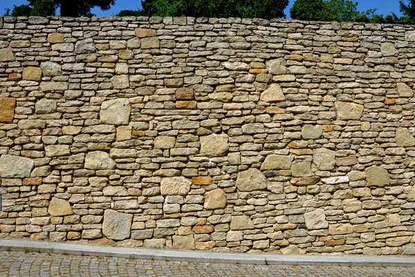 beautifully folded retaining wall with a granite attic with small joints. brown beige yellow irregular gneiss stone holding a slope above it. there are undemanding perennials around