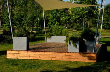 Anaokulundaki oyun parkında, gezinti platformunda güneş ve yağmurun gölgesinde uzanan beyaz tuval. Metalik gri kirişli pergola, kablo, elektrik, ampul,