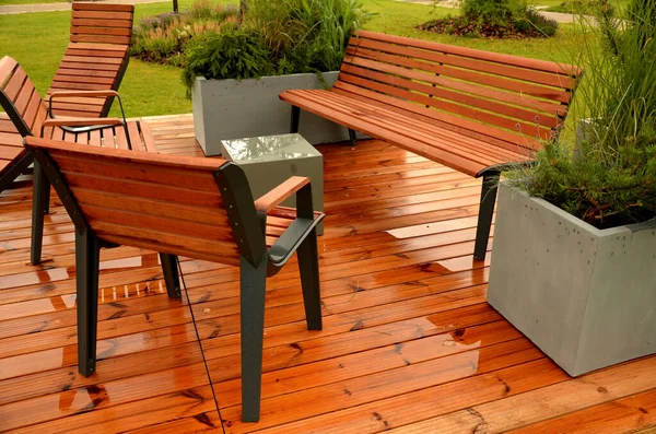 stock image rocking chair on the pavement under the trees in the square. wooden deck chairs made of tropical wood for one person in the park. They are comfortable made of brown planks, slats steel frames, pine