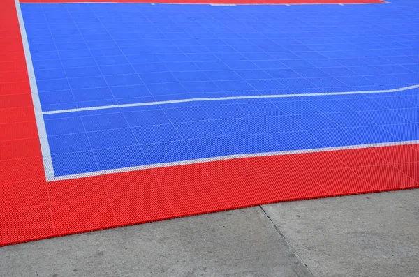 A volleyball court was created in the parking lot. the tiles connected and portable form a red-blue plastic platform on the concrete floor. mattress, plastic grid, rubber, soft