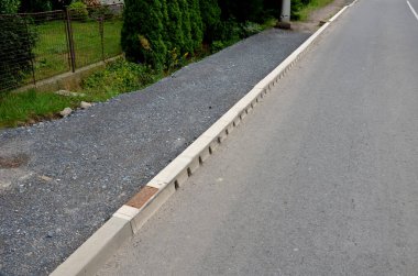 Asfalt yol drenaj sisteminin kenarına gizlenmiş drenaj deliği delinmiş gri bir kaldırıma gizlenmiş. Bütün yol boyunca su kanalizasyona boşalıyor. Deliklerden.