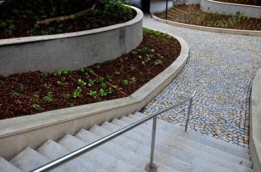 new plantings of perennials in the sloping park with anti-erosion battening. retaining walls cast from concrete in graceful arches. staircase with central railing metal steel, silver