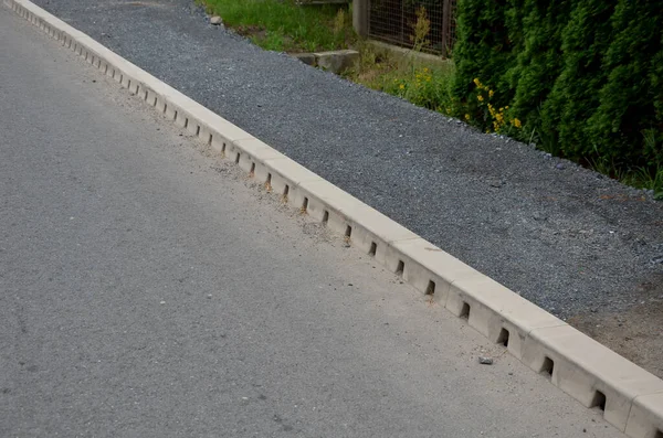 drainage hidden on the edge of an asphalt road Drainage system hidden in a perforated concrete gray curb. the water along the entire length of the road drains into the sewer through holes