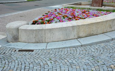 Pembe-turuncu bir çiçek kombinasyonu olan çılgın yıllık yatak. Çeşmenin yanındaki meydanda yuvarlak kum taşından duvarlar var. Sıra dışı bir renk şebekesinde çiçek halıları