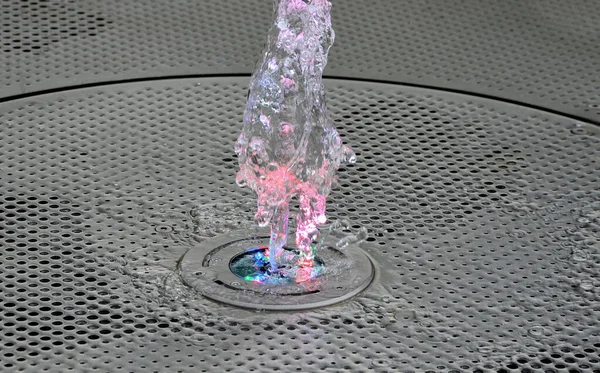 water sprays backlit by colored lights alternating at night with a color range. the water features come directly from the paved square, which is made of stainless steel sheet perforated in a circle