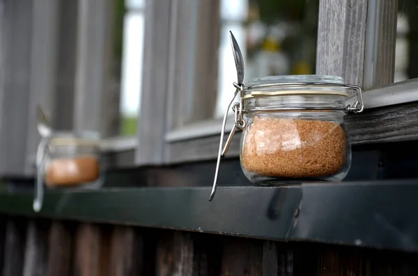 cane sugar in a jar with a spoon ready to use on the cottage terrace window. glass with a rubber band and a seal against moisture. cafe in a family environment. brown sweet powdered sugar