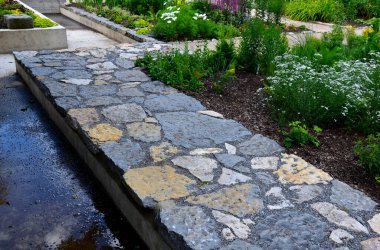 Düzenli şekilli bir göletin üzerindeki parkta kaldırım taşlarının üzerinde yontulmuş kireçtaşı taşları. Yatakları döşeyelim. düz taş karoların gri ve kahverengi karışımı