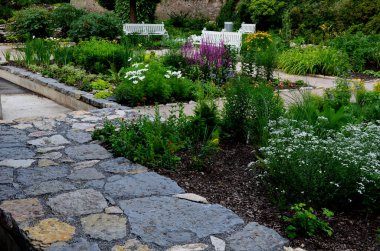 rough-hewn limestone stones on the paving of a path in a park above a regularly shaped pond. tralk beds around. gray and brown mix of flat stone tiles