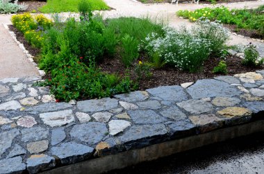 Düzenli şekilli bir göletin üzerindeki parkta kaldırım taşlarının üzerinde yontulmuş kireçtaşı taşları. Yatakları döşeyelim. düz taş karoların gri ve kahverengi karışımı