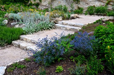 Düzenli şekilli bir göletin üzerindeki parkta kaldırım taşlarının üzerinde yontulmuş kireçtaşı taşları. Yatakları döşeyelim. düz taş karoların gri ve kahverengi karışımı