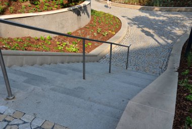 new plantings of perennials in the sloping park with anti-erosion battening. retaining walls cast from concrete in graceful arches. staircase with central railing metal steel, silver
