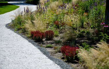 beds of newly planted flowers are planted and mulched with bark. bluebells and cypresses, paths strewn with marble dust twist through the park. supporting granite gabion basket wall, blooming, edge