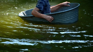 The boys sail on a boat made of old tin, tubs, a bucket, a barrel, a bowl, an oval-shaped flower pot. they fall on the river with their hands. they are children's adventures in the village