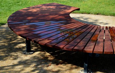 circular bench made of brown-red teak wood. tropical impregnated podia boards for sunbathing visitors in the park. spiral shape, snail shells. trowel base in the lawn, tree, trunk