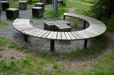 three round benches in the park. the grill is in the middle of sitting. large wood-paneled crescent moon in a meadow under a pergola. massive wooden blocks, terrace, plank, stripes, striped, board