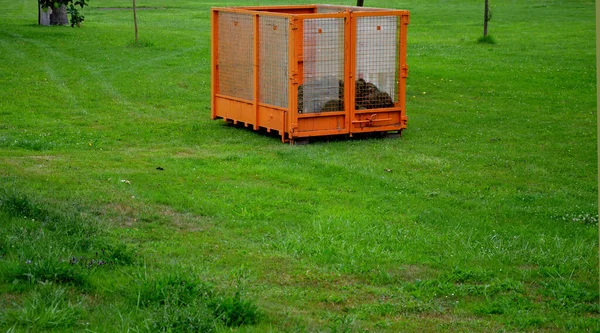 orange container for lawnmower clippings. waste is poured from the bin directly into the mesh box. where it is then taken by the gardening service to the composting plant