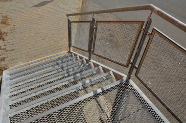 Endüstriyel salonda, ağır yüklenmiş çelik zemin ızgara ve parmaklıkların altında bile yüksek dirençle dolu dik bir merdivenin yan kapısı var. Genişletilmiş metal, güvenlik sarısının kenarları. 