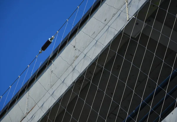 in front of the facade with the balconies is a tensioned cable network covering the entire building. electrical tension insulators. the corners of the building into an arch, rounded. braided network