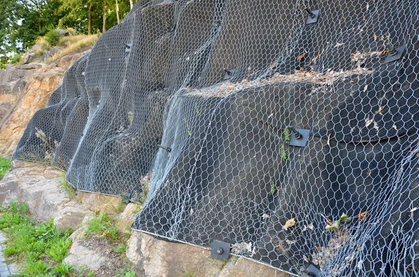 reinforcing slope with steel net anchored deep into rock. falling loose rock stones do not fall on road. anchored with steel nails with nuts. drilled into subsoil and fasten the mesh, train track