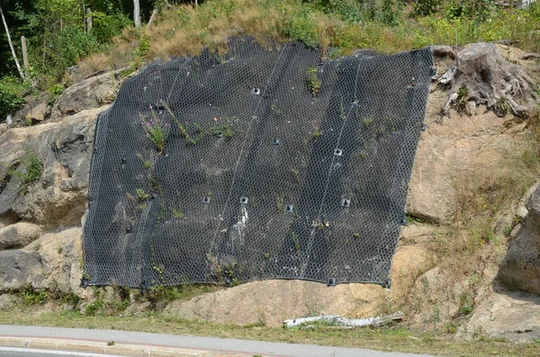 reinforcing slope with steel net anchored deep into rock. falling loose rock stones do not fall on road. anchored with steel nails with nuts. drilled into subsoil and fasten the mesh, train track