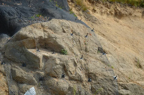 reinforcing slope with steel net anchored deep into rock. falling loose rock stones do not fall on road. anchored with steel nails with nuts. drilled into subsoil and fasten the mesh, train track