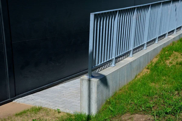 galvanized metal railings at a gray sheet metal industrial hall. concrete gray railing at the ramp. lawn around the building. concrete subfloor