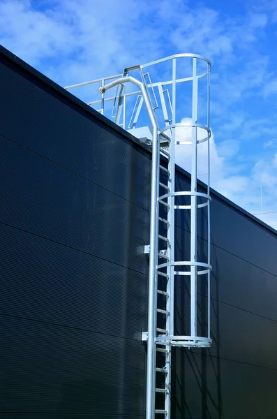 the fire ladder leading to the roof of the hall is secured by a grille in the lower part of the protective grille. white metal warehouse walls. galvanized iron and a pipe for connecting fire hoses