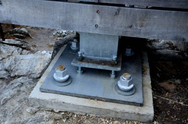 attached to the bridge to the concrete foundation. massive screws hold the steel beam to the ground. adjustment of the seating of the screw on the thread.