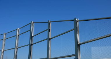 soundproof wall of blue glass on a highway bridge embedded in metal beams, on the street. road traffic noise is reduced. safety protection with steel cables against falling on people, tilt, slanted
