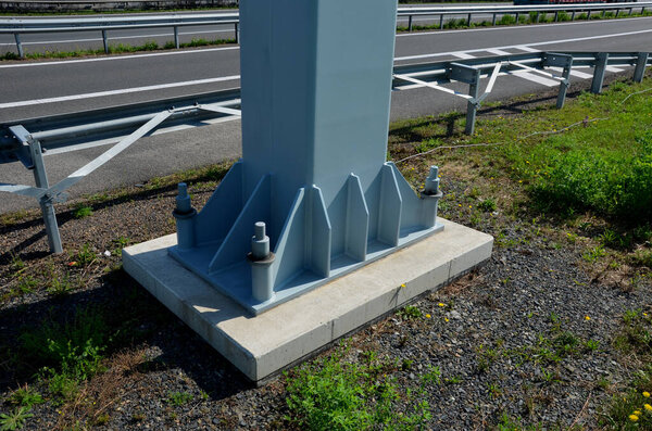 gray steel column, beam, bolted with massive large screws to concrete foundation. ski lift pole, high voltage, billboard advertising in parking lot. cylindrical steel pylon, tube