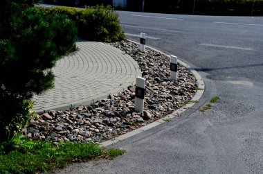 Kavşakta kıvrımlı kaldırımlı bir çiçek tarhı. Yayalar yaya geçidinden geçiyorlar. Ok araçları otoyol çıkışındaki doğru şeride yönlendiriyor.