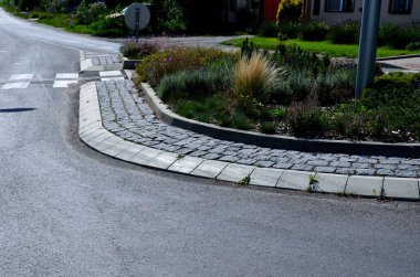 Kavşakta kıvrımlı kaldırımlı bir çiçek tarhı. Yayalar yaya geçidinden geçiyorlar. Ok araçları otoyol çıkışındaki doğru şeride yönlendiriyor.