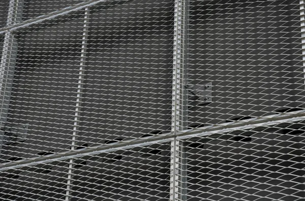 steel cladding of a building with a expanded metal lattice structure. galvanized gray nets protect the industrial building. Blue sky in contrast to a silver background, wall