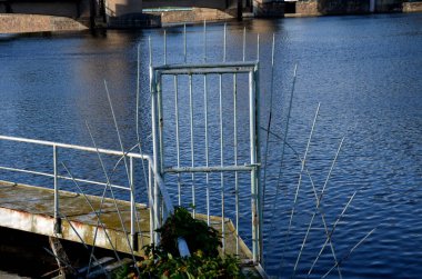 Suyun üzerindeki köprü çivili çitleri olan bir kapı tarafından korunuyor. Beyaz metal eskrim, özel tekneler için rıhtım iskelesi. İzinsiz girişe karşı güvenli yol