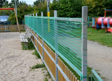 Çocukların oyun parkının çitlerle çevrili olması ve çitin üstünde bir ağ daha olması. Galvanize metal çerçeve yeşil bir tekstil örgüsüyle çitin yüksekliğini arttırır. kum kutusu